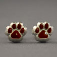 A pair of silver-colored paw print earrings with maroon accents, displayed against a white background.