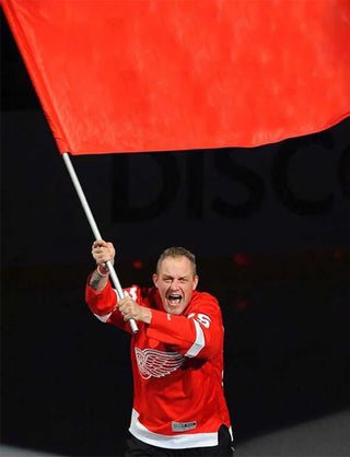 A person wearing a red sports jersey is holding a red flag on a pole, celebrating.
